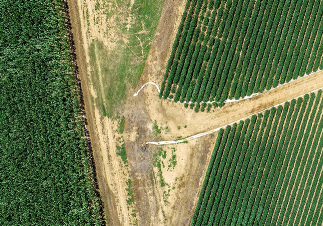 An aerial image of multiple crops fields intersecting with white poly-pipe on the field edge